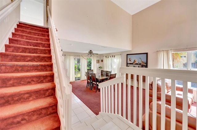 stairway featuring carpet flooring, ceiling fan, and a towering ceiling