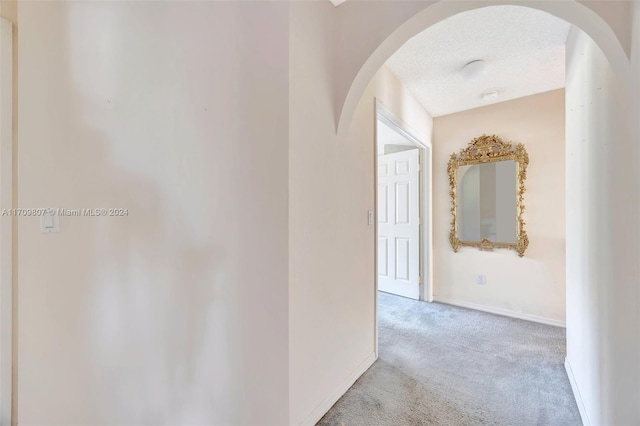 corridor featuring light carpet and a textured ceiling