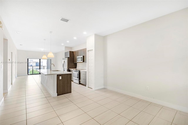 kitchen with sink, light tile patterned floors, an island with sink, appliances with stainless steel finishes, and decorative light fixtures