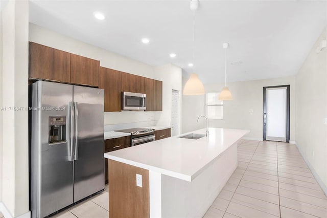 kitchen with appliances with stainless steel finishes, sink, light tile patterned floors, pendant lighting, and an island with sink