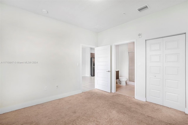 unfurnished bedroom featuring ensuite bath, light carpet, a closet, and stainless steel refrigerator with ice dispenser