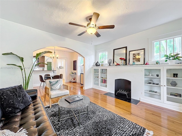 living room with ceiling fan with notable chandelier, wood-type flooring, a fireplace, and a wealth of natural light