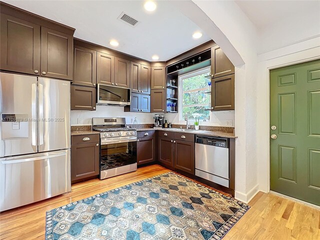 kitchen featuring dark stone countertops, dark brown cabinetry, light wood-type flooring, and appliances with stainless steel finishes