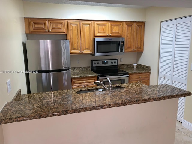 kitchen with dark stone countertops, sink, light tile patterned floors, and stainless steel appliances