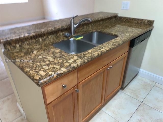 kitchen with dishwasher, light tile patterned flooring, dark stone counters, and sink