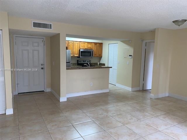 kitchen with kitchen peninsula, light tile patterned floors, a textured ceiling, and stainless steel appliances