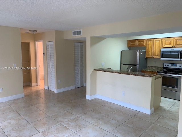 kitchen featuring a textured ceiling, stainless steel appliances, dark stone counters, and light tile patterned flooring