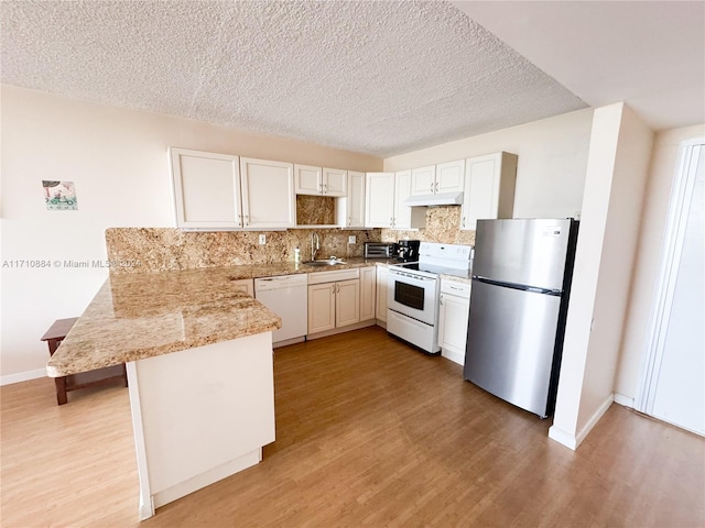 kitchen with sink, a kitchen breakfast bar, kitchen peninsula, white appliances, and light wood-type flooring