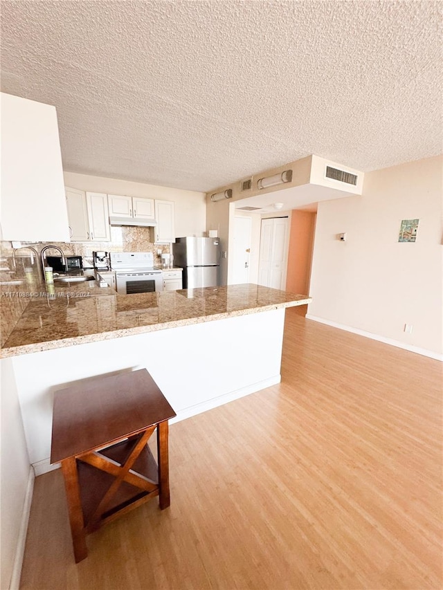 kitchen with kitchen peninsula, a textured ceiling, white stove, and stainless steel refrigerator