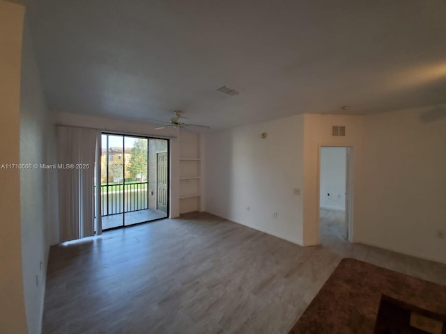 empty room with built in features, visible vents, light wood-style flooring, and a ceiling fan