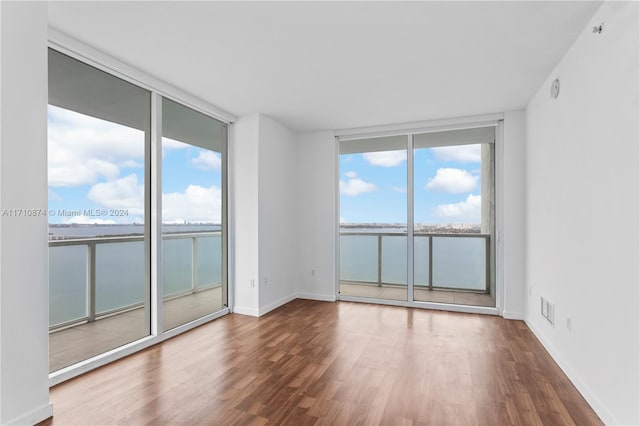 spare room with wood-type flooring, a water view, and floor to ceiling windows