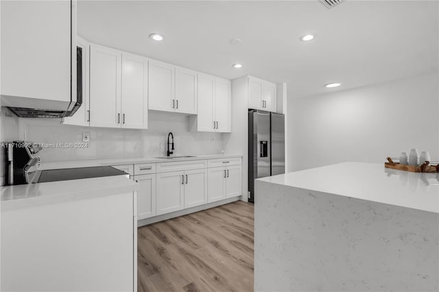 kitchen featuring stainless steel refrigerator with ice dispenser, light wood-type flooring, stove, sink, and white cabinets