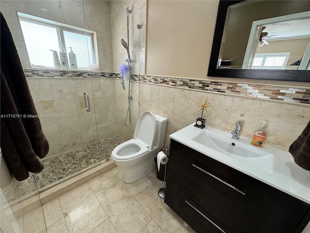 bathroom featuring ceiling fan, toilet, vanity, a shower with shower door, and tile walls