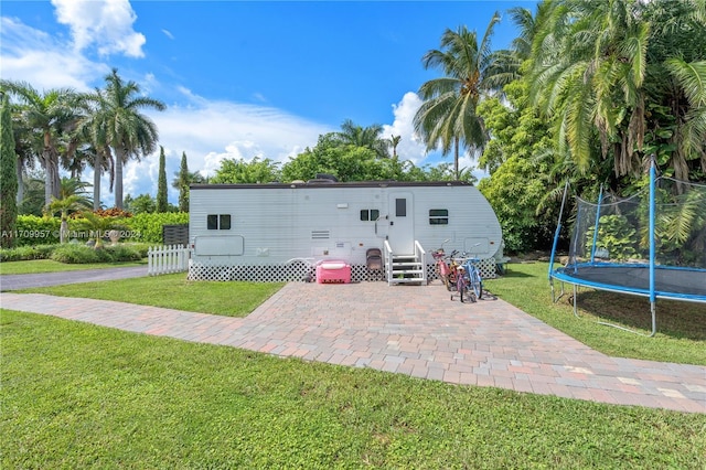 rear view of property featuring a patio, a trampoline, and a lawn