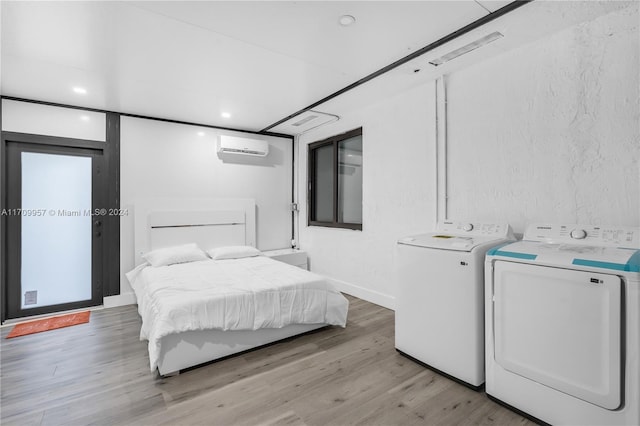 bedroom featuring washer and clothes dryer, light hardwood / wood-style flooring, and an AC wall unit