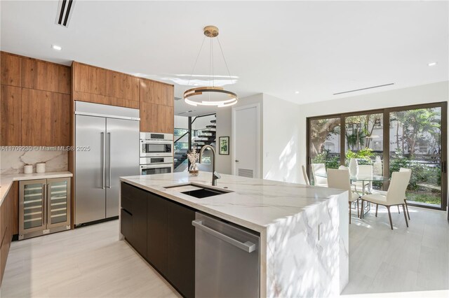 kitchen featuring sink, light stone countertops, an island with sink, decorative light fixtures, and stainless steel appliances