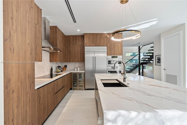 kitchen featuring sink, wall chimney exhaust hood, stainless steel appliances, hanging light fixtures, and beverage cooler