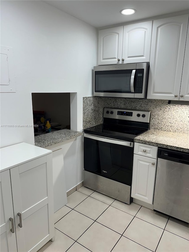 kitchen with light stone countertops, backsplash, stainless steel appliances, light tile patterned floors, and white cabinetry