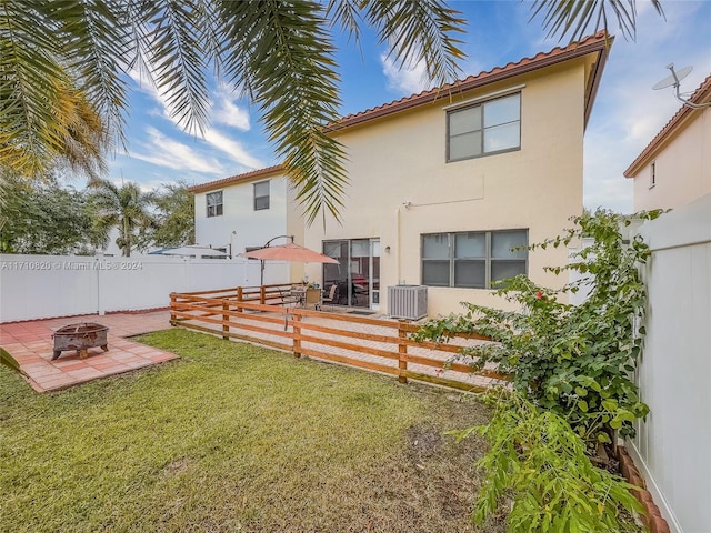 rear view of property with a lawn, cooling unit, a patio, and a fire pit