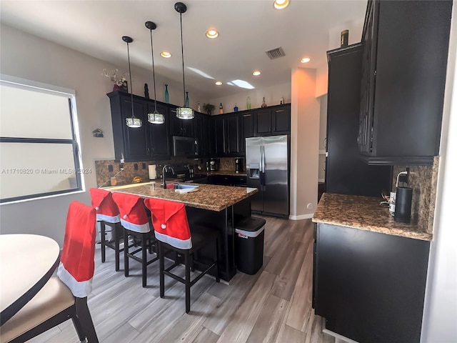 kitchen with tasteful backsplash, pendant lighting, a breakfast bar, appliances with stainless steel finishes, and light wood-type flooring