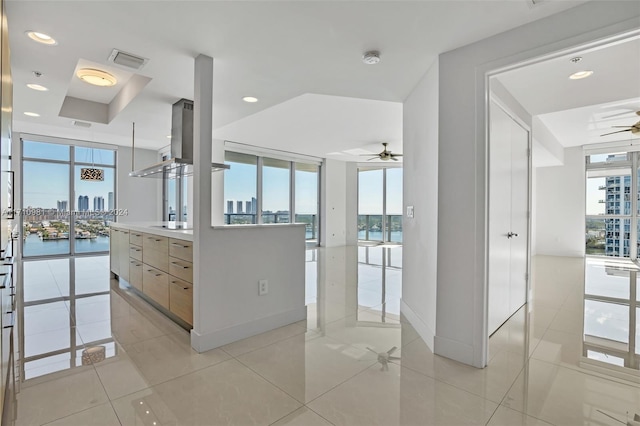 kitchen with floor to ceiling windows, light brown cabinetry, a water view, light tile patterned floors, and ceiling fan