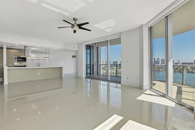 unfurnished living room with floor to ceiling windows, a water view, light tile patterned floors, and ceiling fan