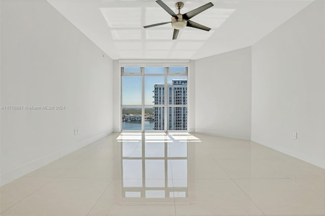 tiled spare room with ceiling fan, a water view, and a wall of windows