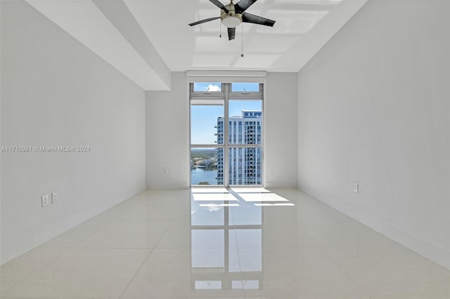 empty room with a water view, ceiling fan, expansive windows, and light tile patterned floors