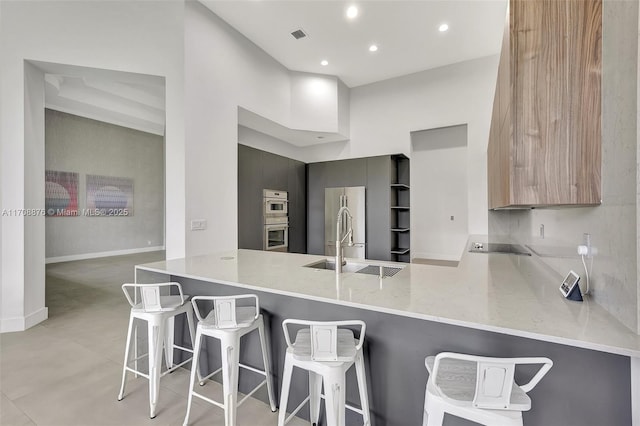 kitchen featuring a towering ceiling, appliances with stainless steel finishes, a sink, modern cabinets, and a peninsula