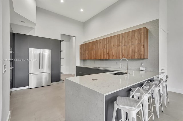 kitchen with a peninsula, a sink, backsplash, freestanding refrigerator, and modern cabinets