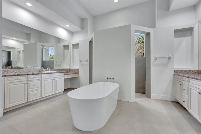 bathroom featuring two vanities, a freestanding tub, a healthy amount of sunlight, and a sink