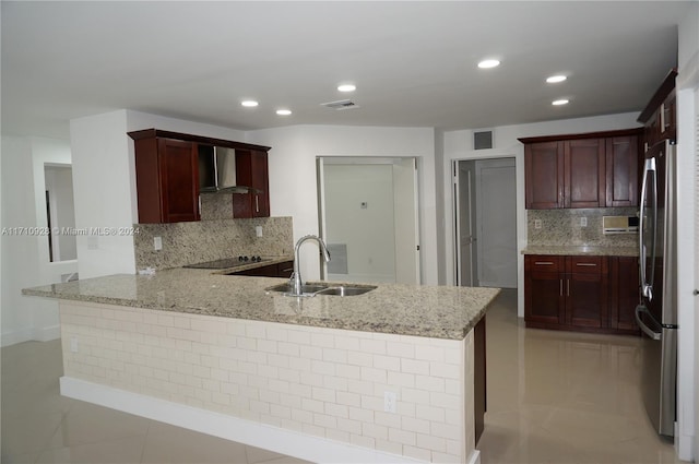 kitchen with wall chimney range hood, sink, decorative backsplash, kitchen peninsula, and stainless steel refrigerator