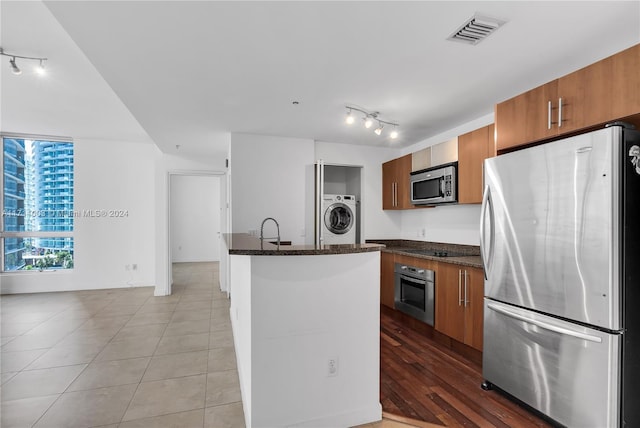 kitchen with sink, dark stone countertops, appliances with stainless steel finishes, light hardwood / wood-style floors, and washer / dryer