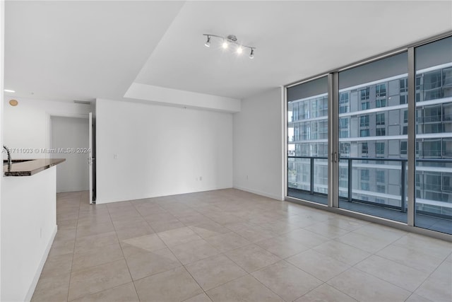 spare room featuring sink, light tile patterned floors, and a wall of windows