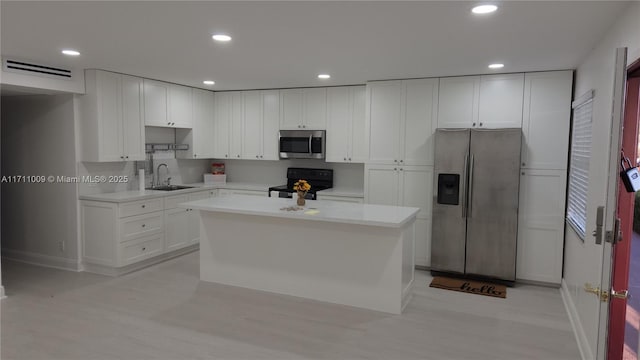 kitchen featuring light hardwood / wood-style flooring, appliances with stainless steel finishes, sink, white cabinets, and a kitchen island