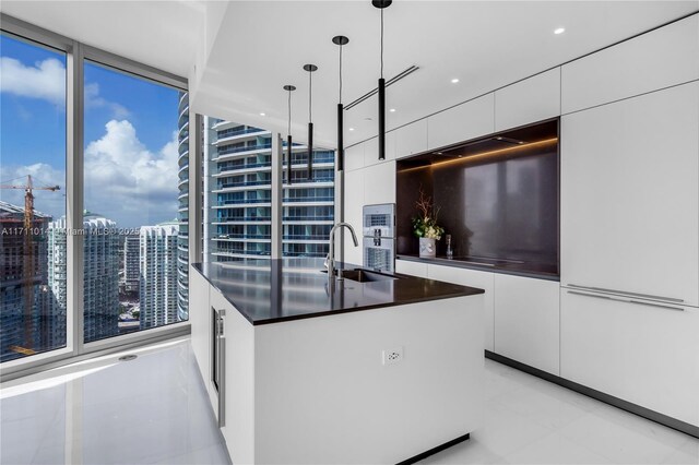 kitchen featuring floor to ceiling windows, sink, light tile patterned floors, hanging light fixtures, and white cabinets