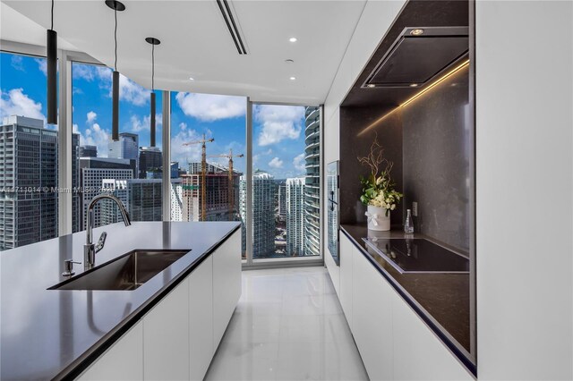 kitchen featuring hanging light fixtures, a wall of windows, sink, and white cabinets