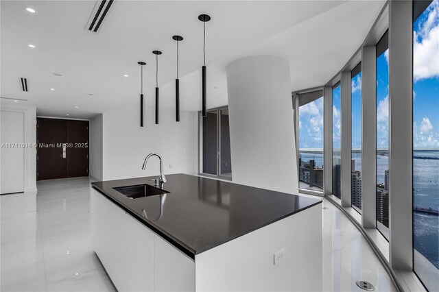 kitchen featuring sink, hanging light fixtures, expansive windows, a water view, and white cabinets