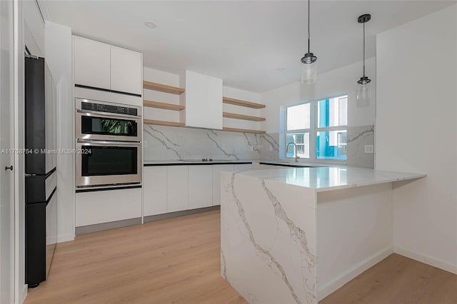 kitchen with white cabinets, stainless steel double oven, decorative light fixtures, and light hardwood / wood-style floors