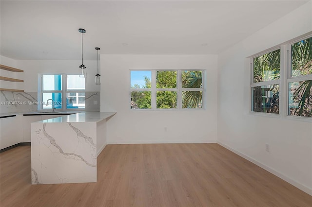 kitchen with white cabinetry, hanging light fixtures, light stone counters, light hardwood / wood-style flooring, and kitchen peninsula