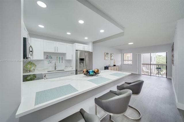 kitchen featuring stainless steel appliances, light hardwood / wood-style flooring, kitchen peninsula, a kitchen bar, and white cabinets