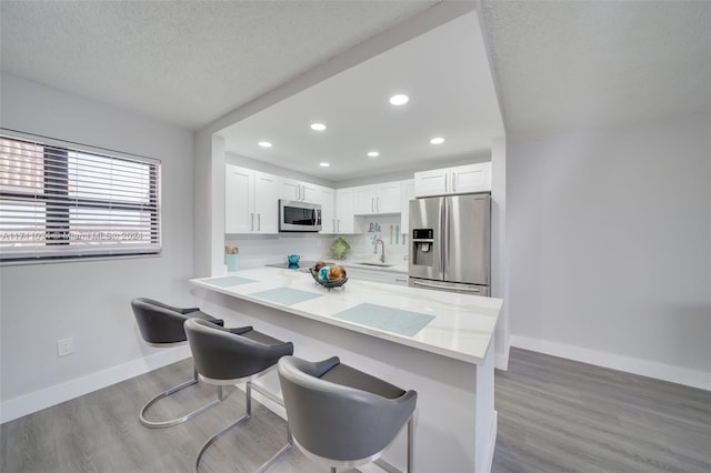 kitchen with light hardwood / wood-style flooring, appliances with stainless steel finishes, white cabinetry, kitchen peninsula, and a breakfast bar area