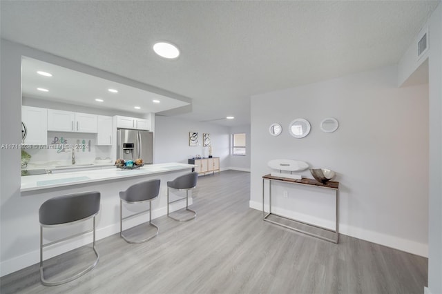 kitchen featuring white cabinetry, a kitchen breakfast bar, stainless steel fridge with ice dispenser, light hardwood / wood-style flooring, and kitchen peninsula