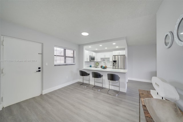 kitchen with kitchen peninsula, white cabinetry, stainless steel appliances, and light hardwood / wood-style flooring