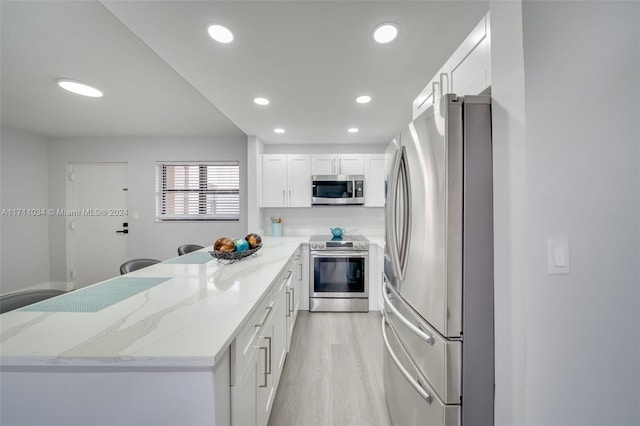 kitchen featuring light stone counters, white cabinets, stainless steel appliances, and light wood-type flooring