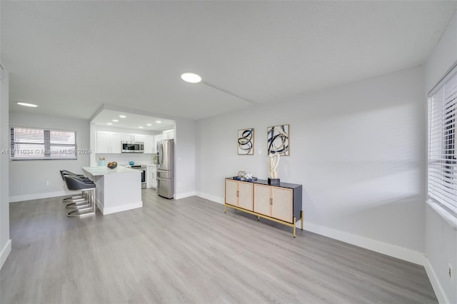 kitchen featuring a kitchen breakfast bar, white cabinetry, light wood-type flooring, and appliances with stainless steel finishes