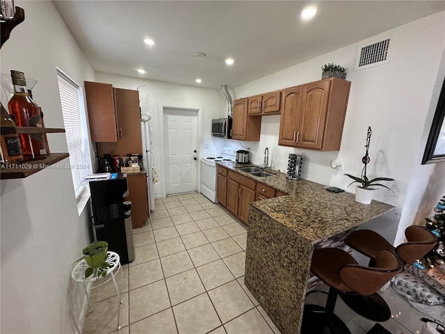 kitchen featuring sink, dark stone counters, white appliances, a kitchen bar, and light tile patterned floors