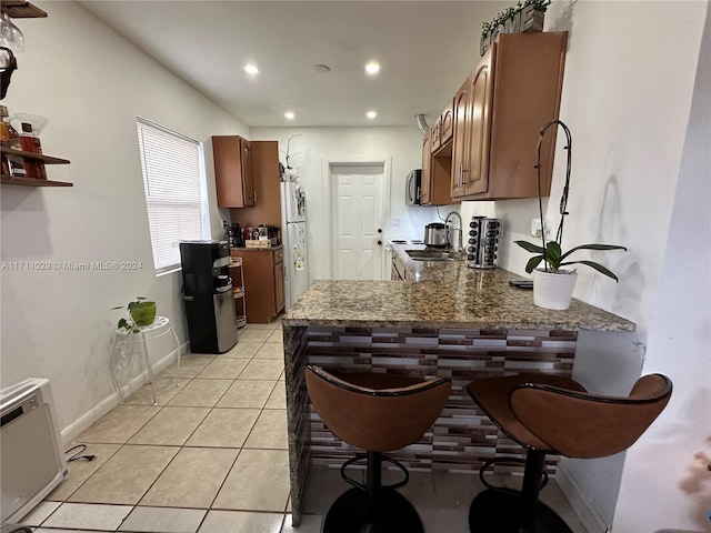 kitchen with dark stone countertops, kitchen peninsula, light tile patterned flooring, and white fridge