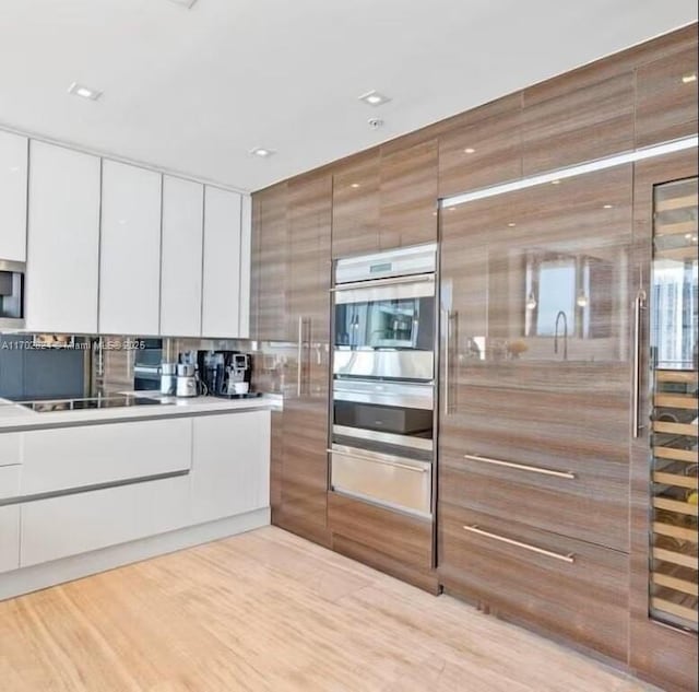 kitchen featuring black electric stovetop, tasteful backsplash, double oven, light hardwood / wood-style floors, and white cabinetry