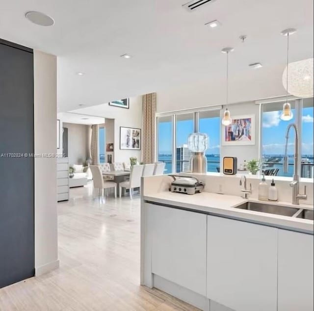 kitchen featuring white cabinets, decorative light fixtures, a water view, and sink